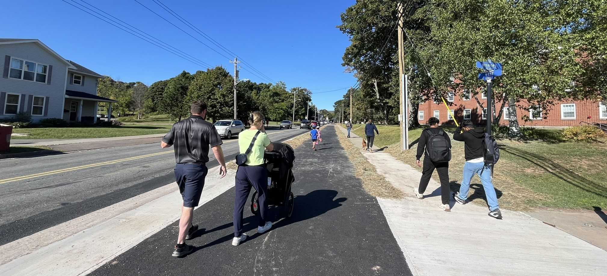 Image showing landscape view of the section of Active Transportation Trail from James Street to Highland Drive, along West Street in the Town of Antigonish. Included in the picture are people walking and pushing a stroller along the trail.